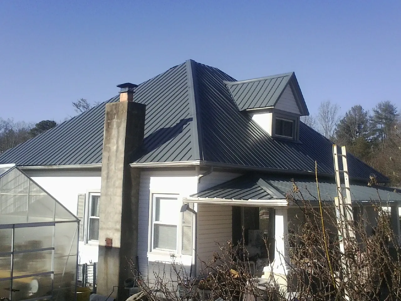 Dark blue standing seam metal roof on a white farmhouse with dormer — Slate & Tile Roof Repair by Roofing Brothers in Cedar Run