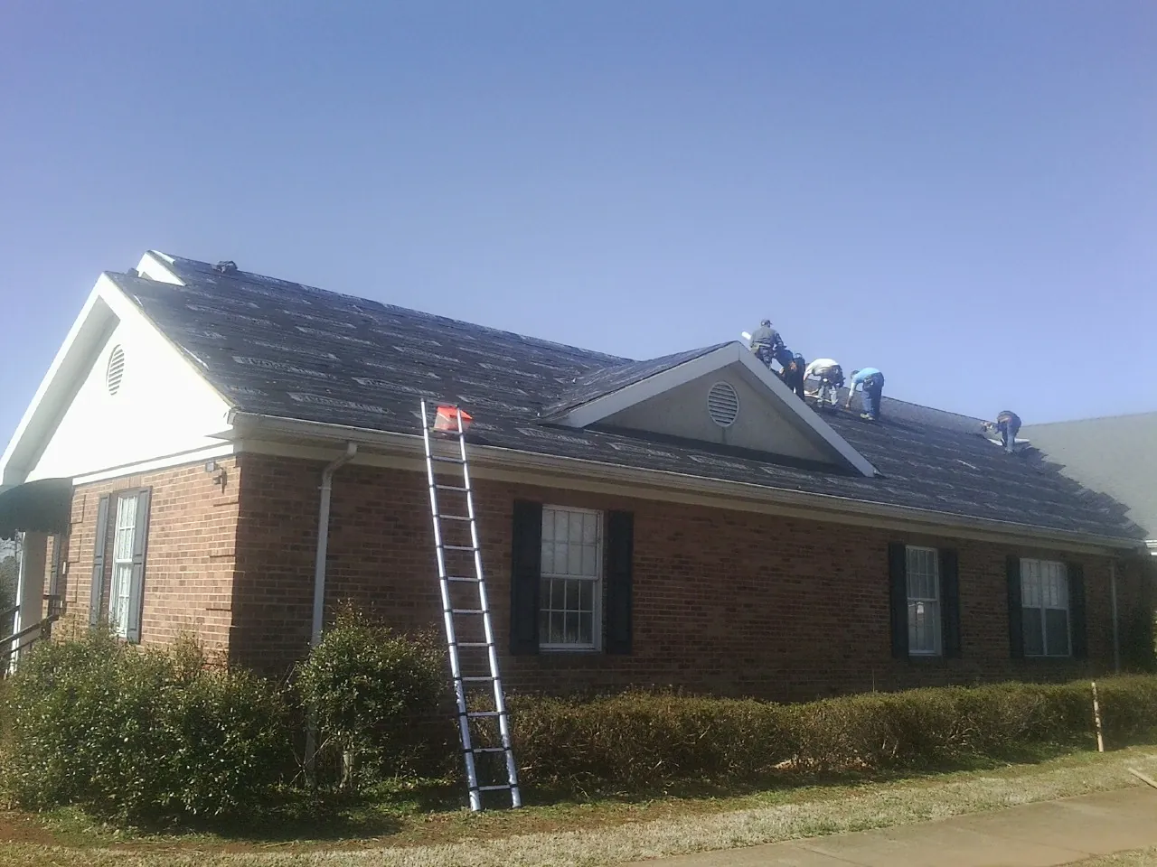 Crew tearing shingles off a brick ranch roof with a ladder set — Emergency Roof Repair work by our crew in Cedar Run