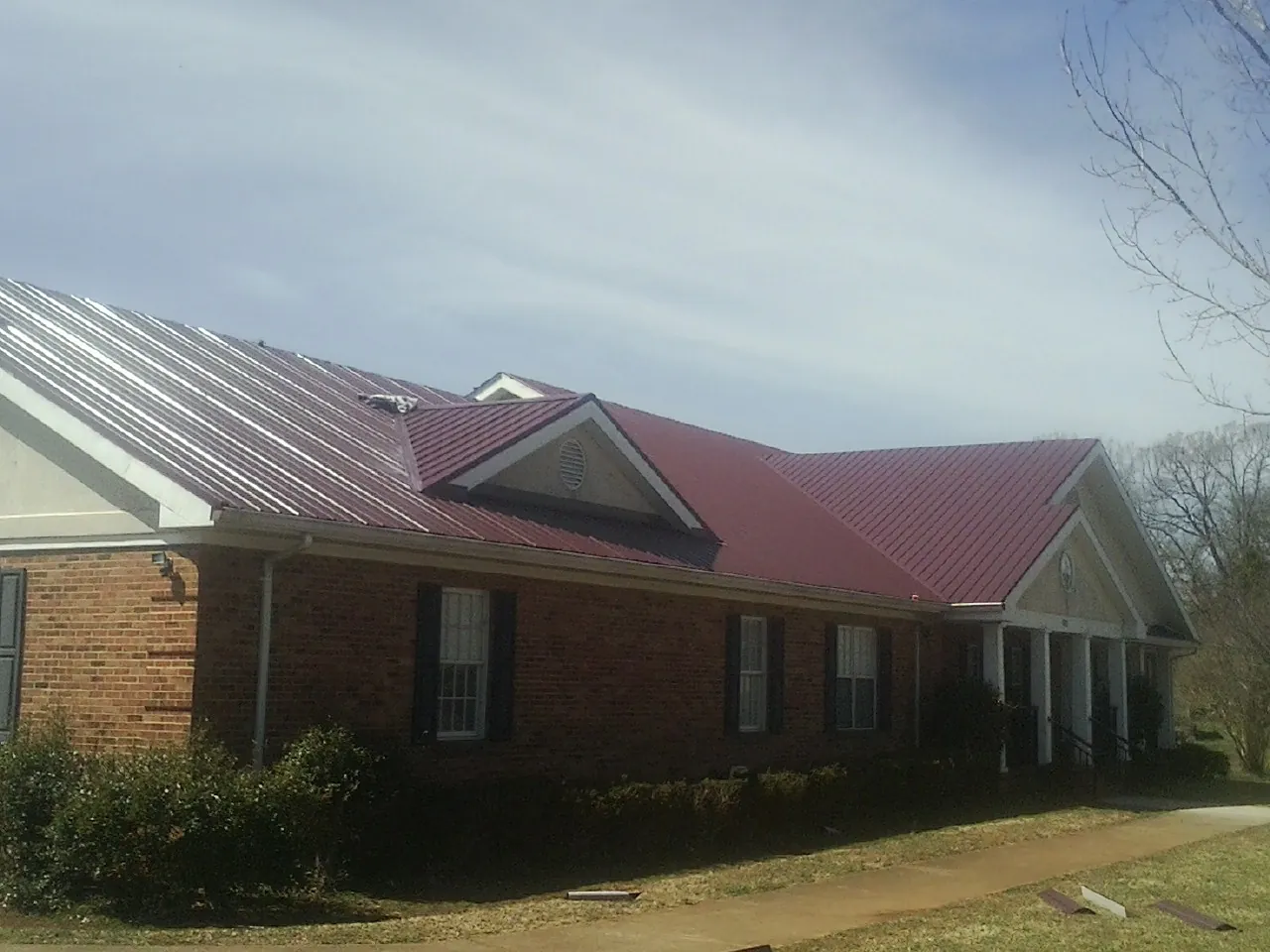 Red metal roof with gabled entries on a long brick building, from a Hail Damage Roof Repair job in Cedar Run