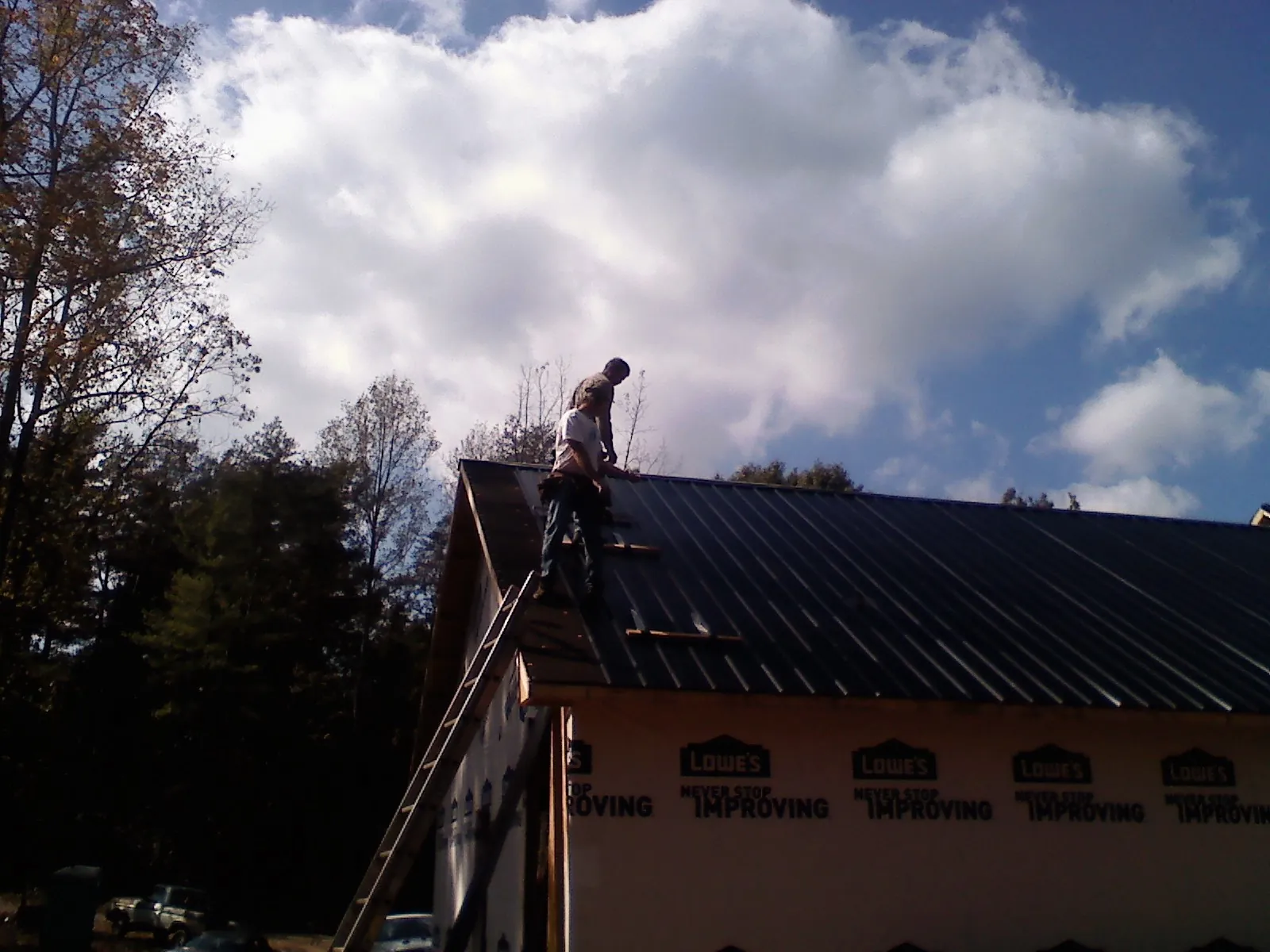 Roofer fastening dark metal panels high against a cloudy sky, from a Roof Inspection job in Cedar Run