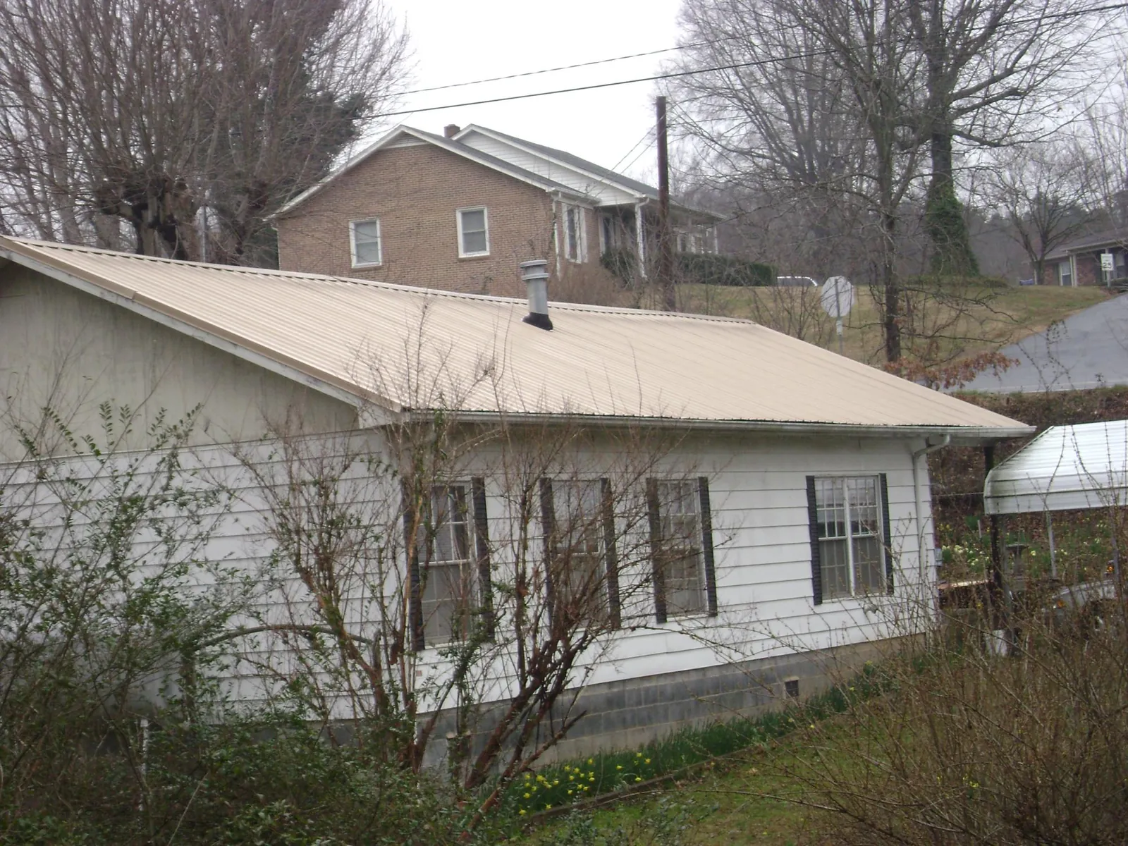 Tan metal roof on a white sided house set into a hillside — Commercial Roofing by Roofing Brothers in Cedar Run